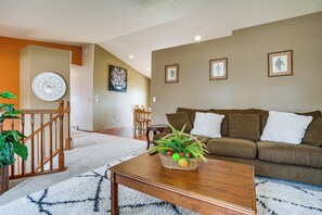 A living room with a wooden coffee table, a brown sofa, a white clock, and framed artwork on the wall.
