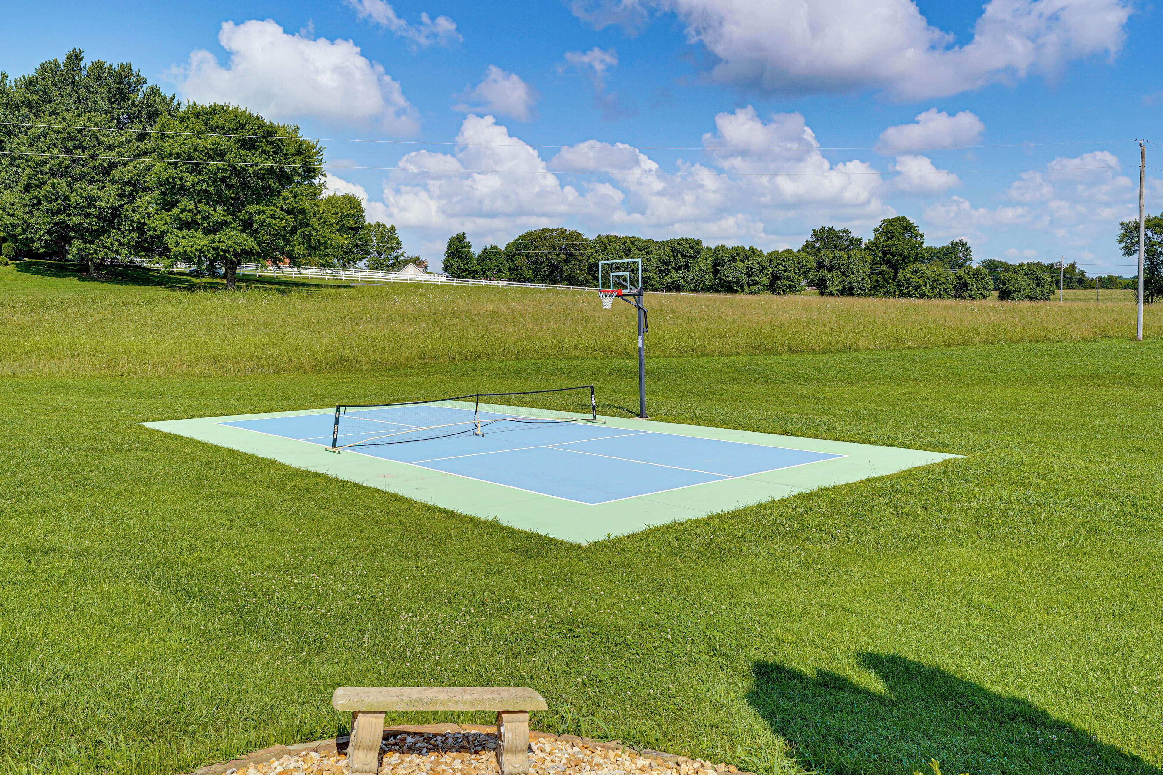 An outdoor basketball court with a wooden bench in the foreground.