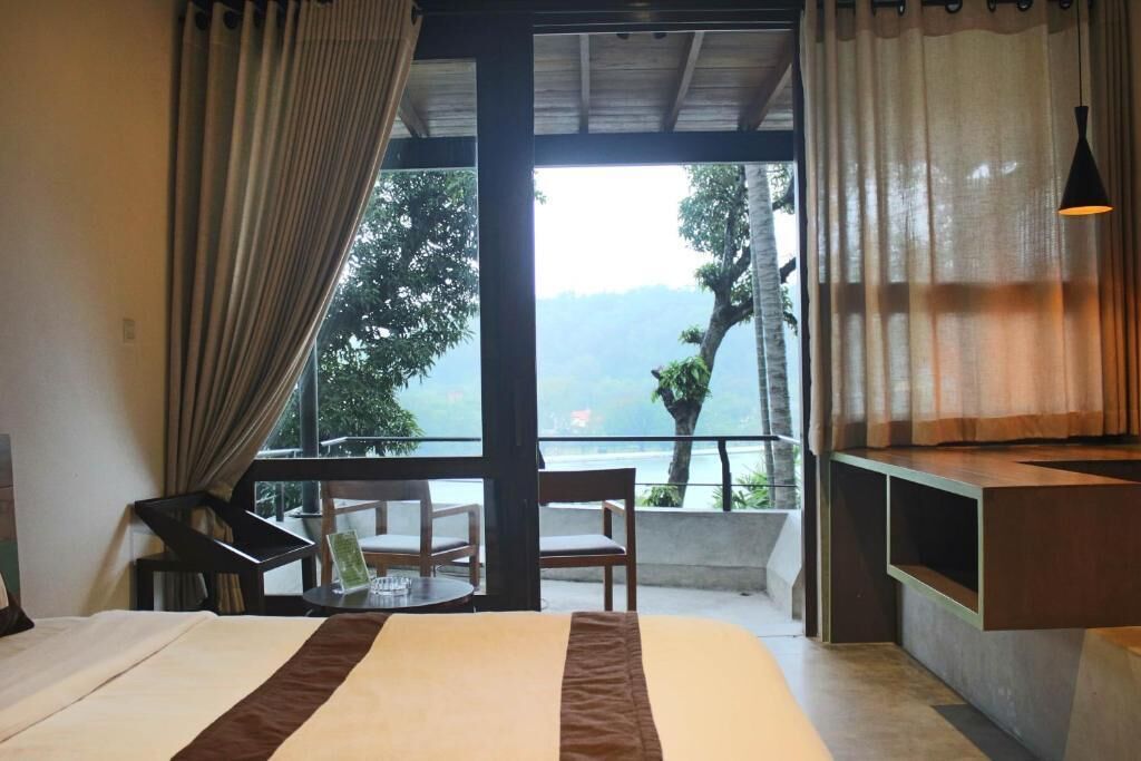 A hotel room with a bed, a desk, a chair, and a balcony with a view of the landscape.