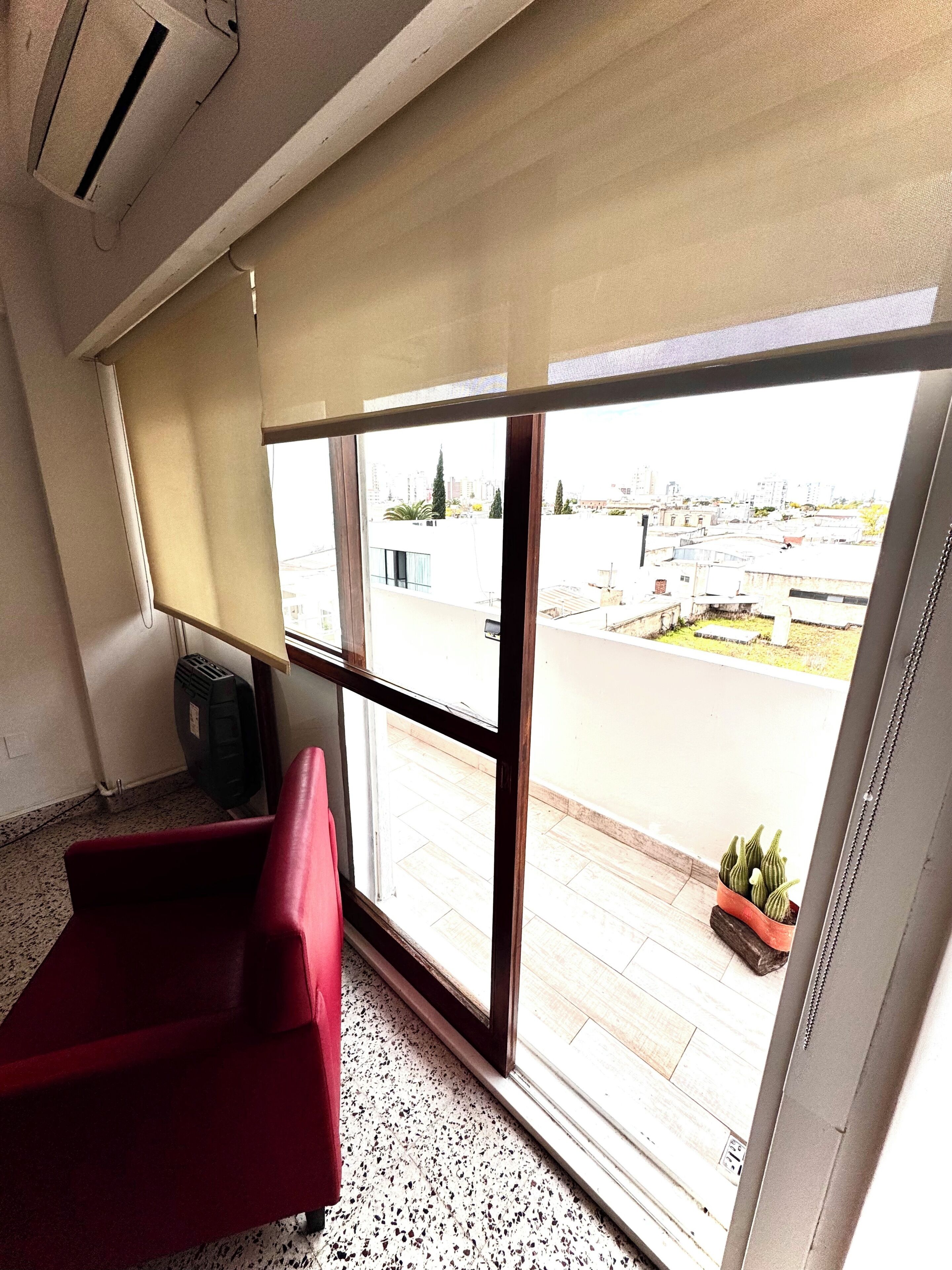 A room with a red chair, a window with a view of a cityscape, and a potted plant on the windowsill.