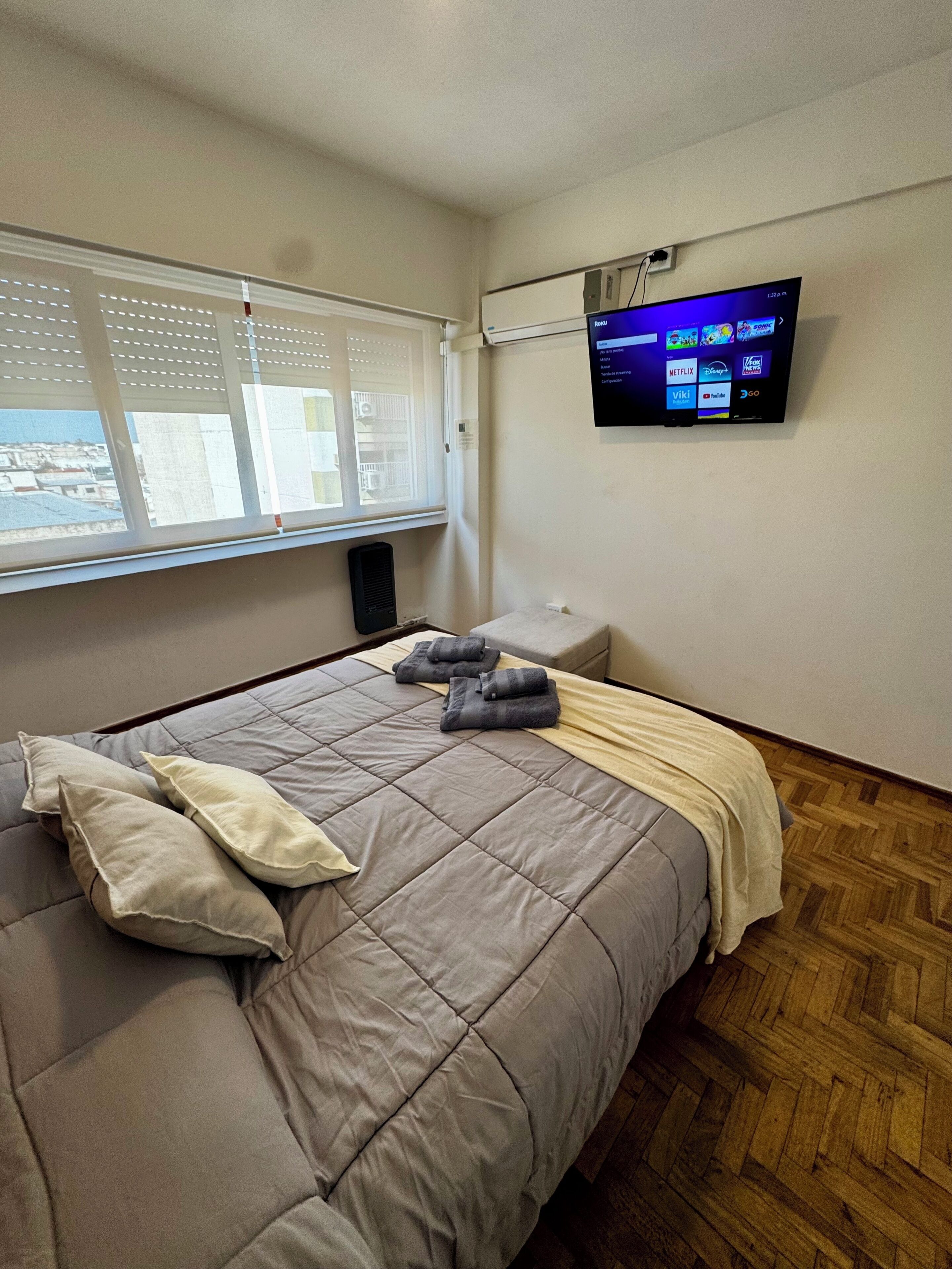 A hotel room with a bed, a TV mounted on the wall, and a window with blinds.