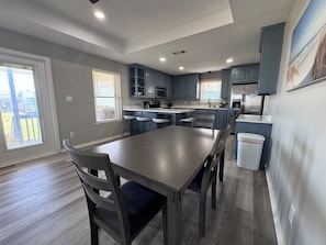 A modern kitchen with grey cabinets, a dining table with chairs, and a view of the outdoors. - Super Cute 2 bedroom, close to beach, affordable! (Crystal Beach)