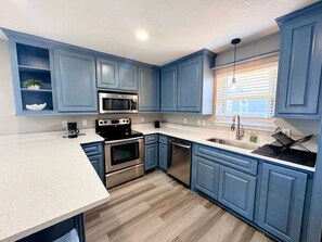 A kitchen with blue cabinets, stainless steel appliances, a white countertop, and a window with blinds. - Super Cute 2 bedroom, close to beach, affordable! (Crystal Beach)