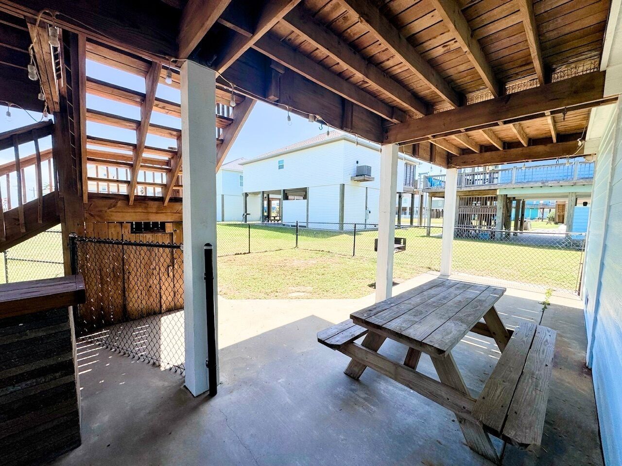 An outdoor covered patio with a wooden table and benches, a concrete floor, and a view of a building in the background.