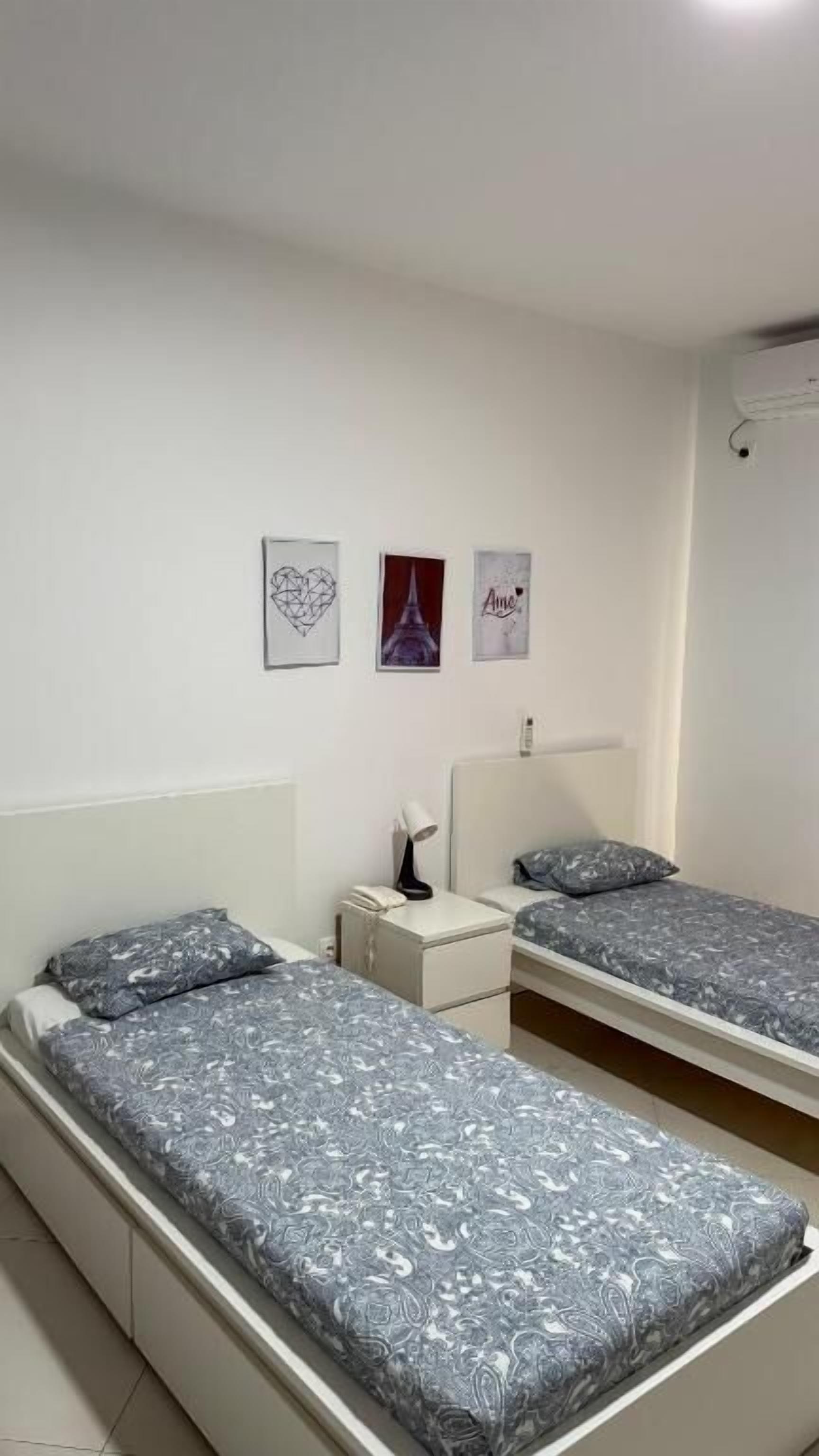 A room with two single beds, a bedside table with a lamp, and three framed pictures on the wall.
