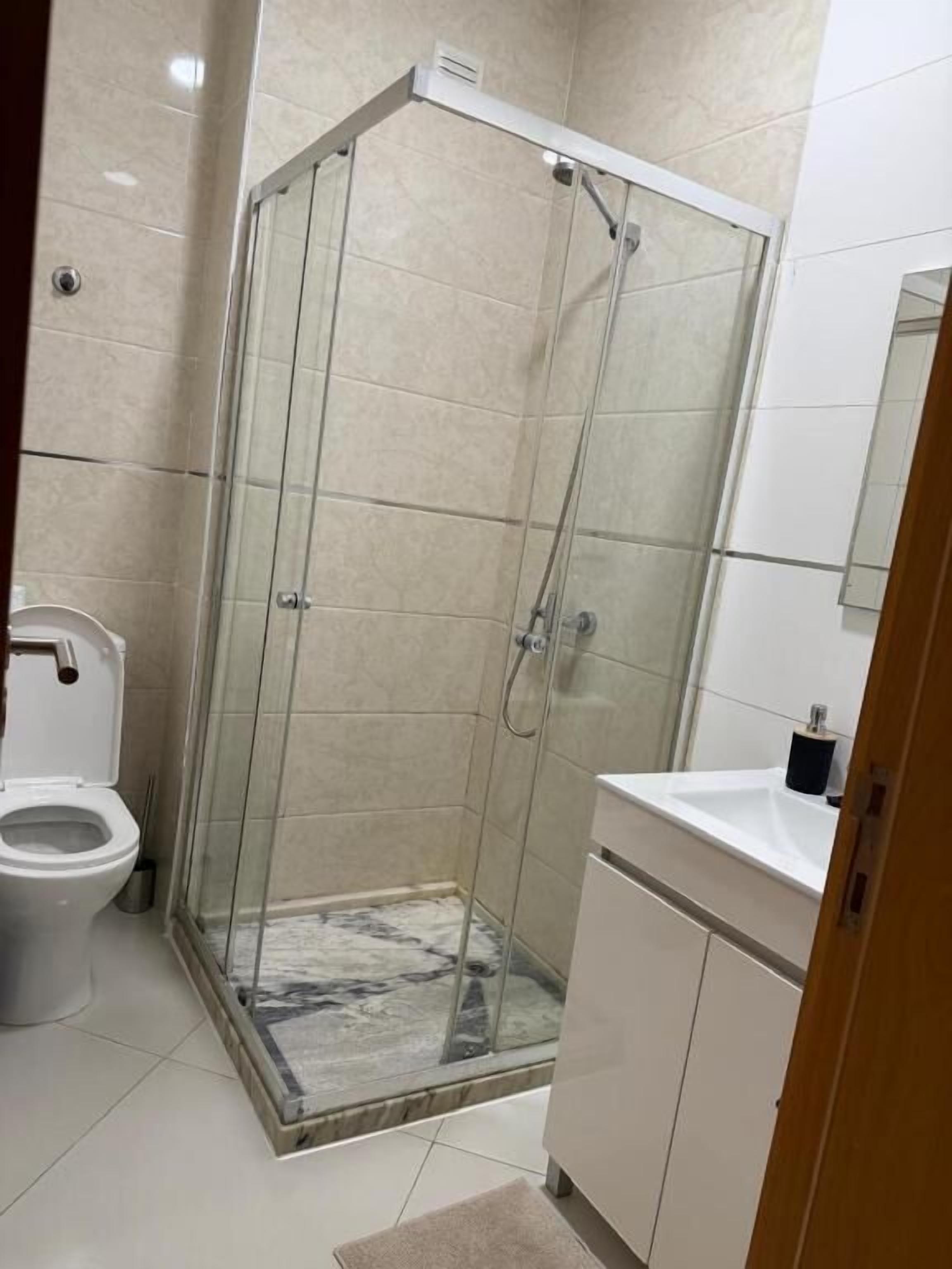 A bathroom with a glass-enclosed shower, a toilet, and a sink.