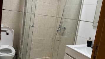 A bathroom with a glass-enclosed shower, a toilet, and a sink.