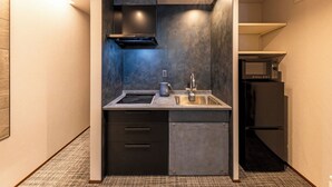 A compact kitchen with a built-in stove, sink, and a microwave. - Asobiyado Rin (Kagoshima-shi)