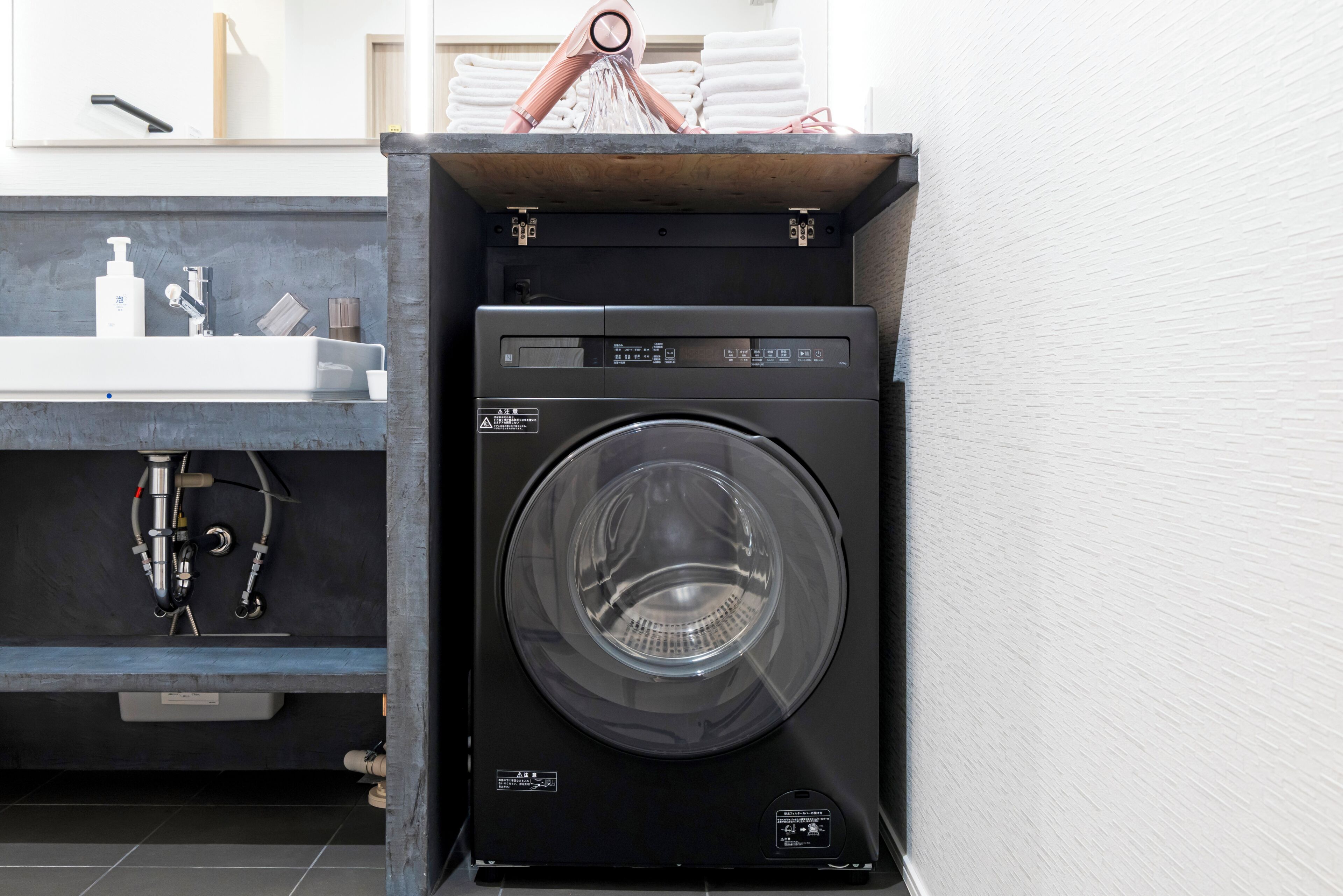 A compact, modern laundry room with a built-in washer and dryer, a sink with a soap dispenser, and a towel rack.