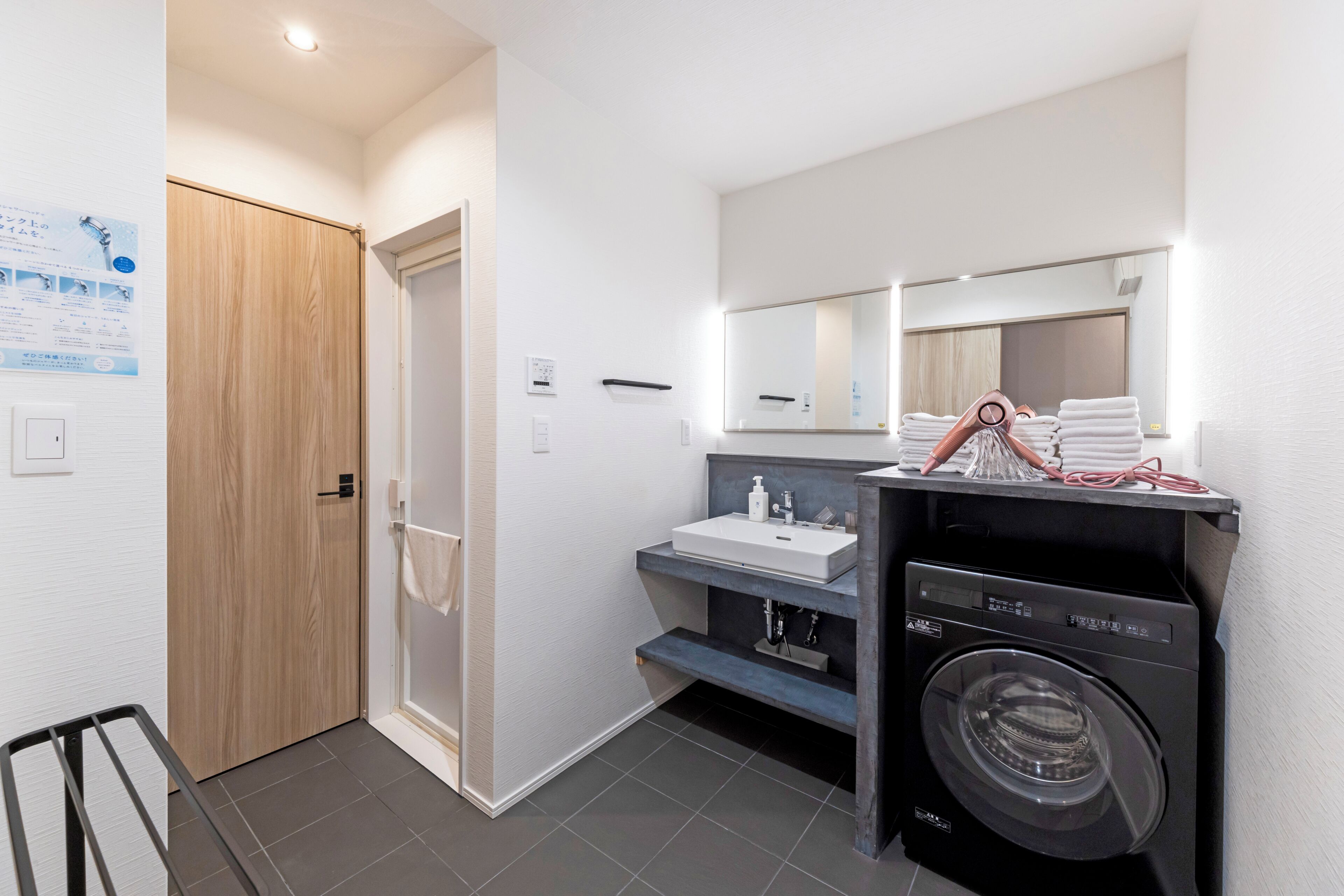 A modern bathroom with a wooden door, a sink with a mirror, and a washing machine.