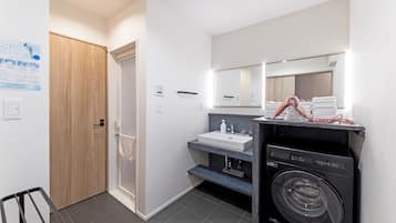 A modern bathroom with a wooden door, a sink with a mirror, and a washing machine.