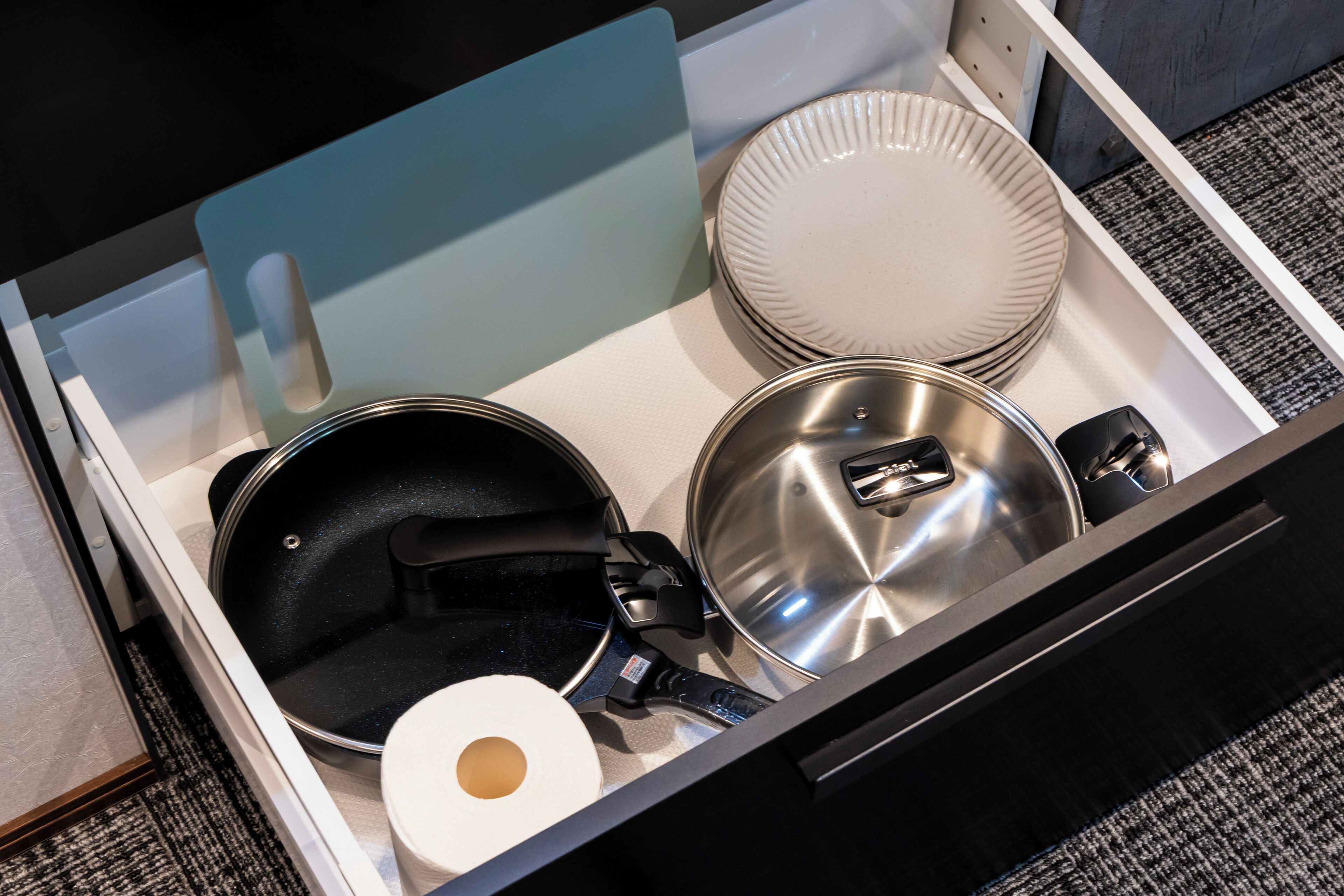 Un cassetto della cucina con pentole e utensili, tra cui una padella, una pentola e un coperchio.