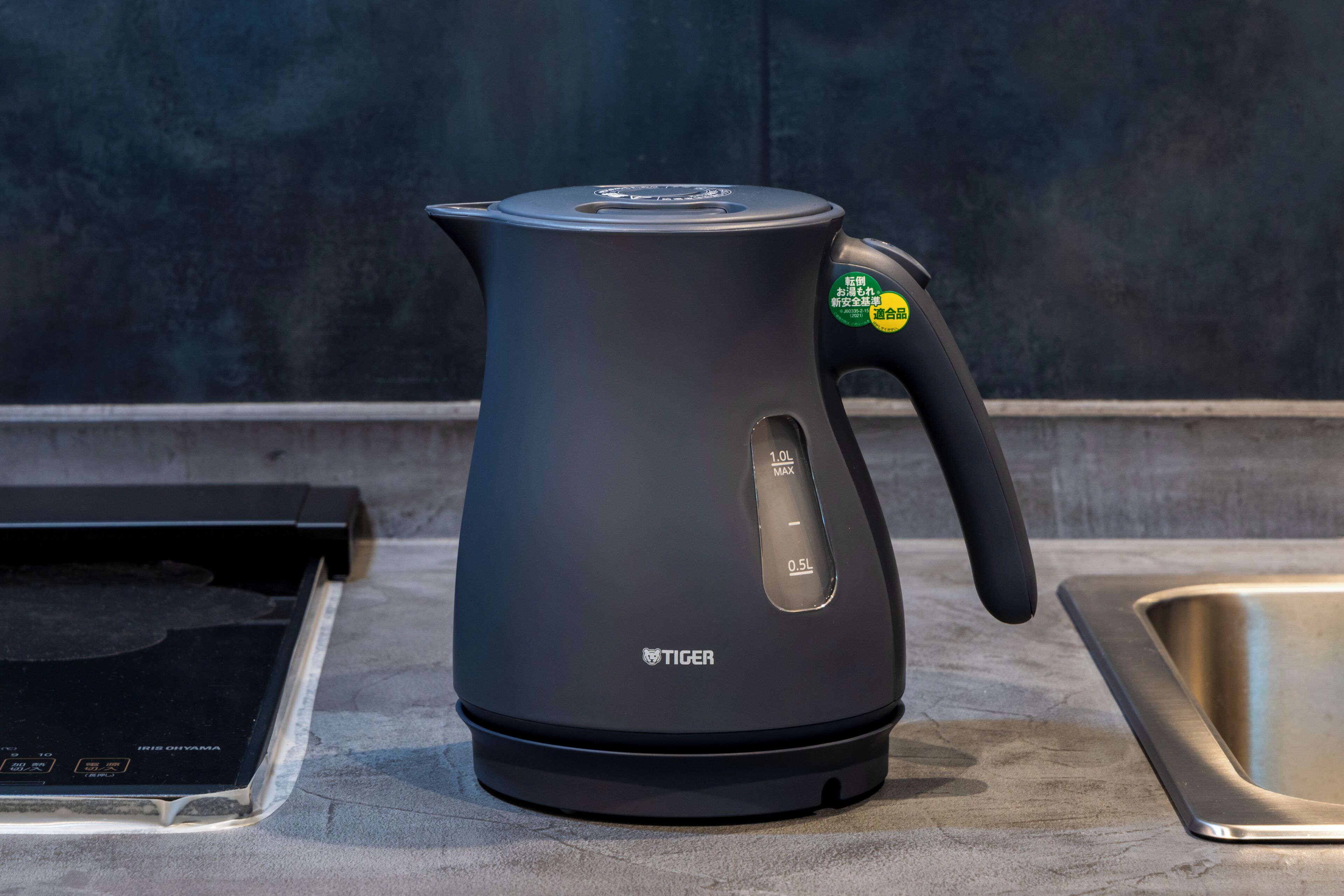 Una tetera eléctrica negra con asa y pantalla digital sobre una encimera de cocina.