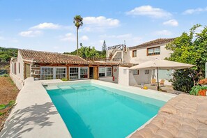 Una casa de dos pisos con piscina, un patio con mesa y sillas, y vistas al paisaje circundante.