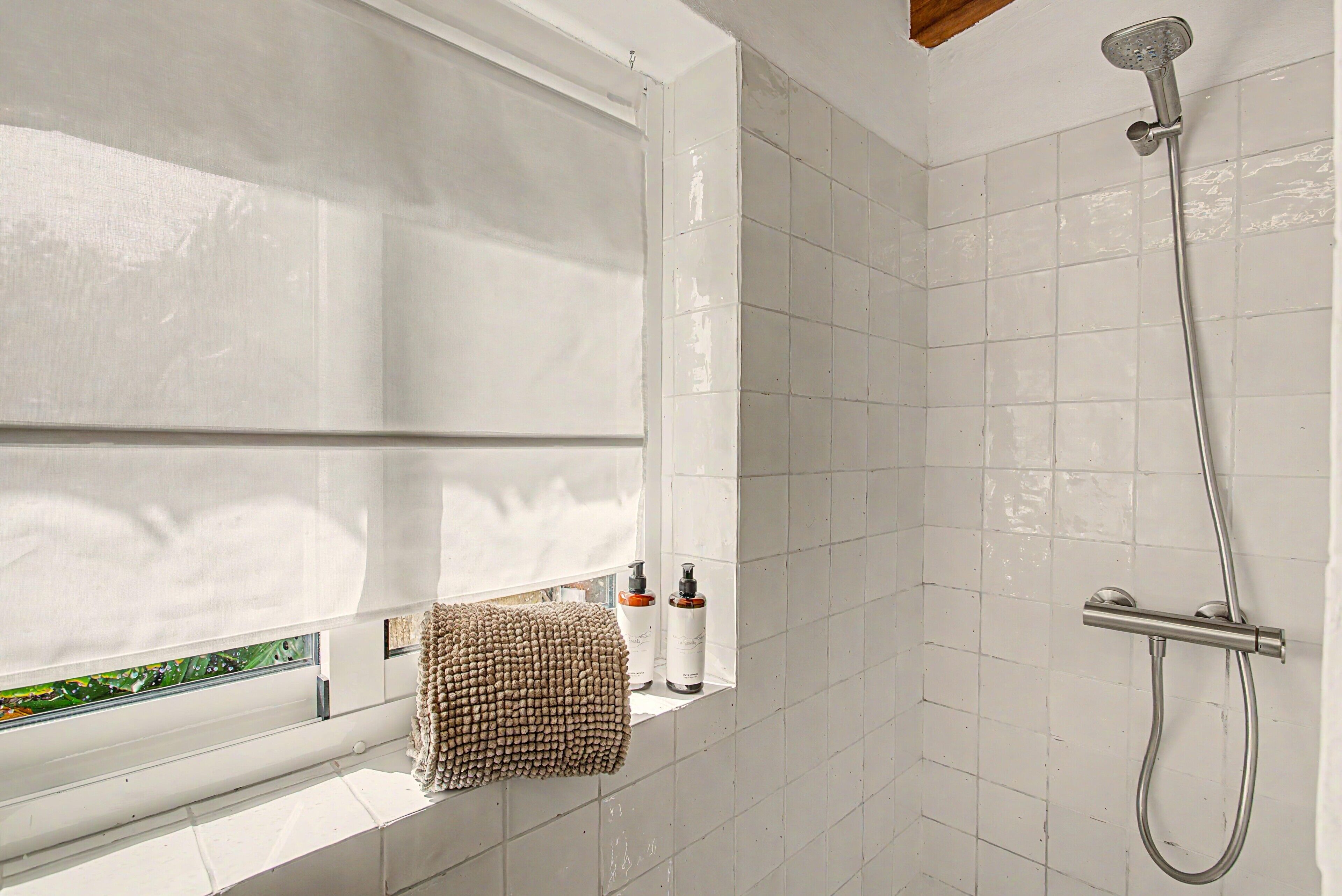 A bathroom with a shower, a window with a towel, and toiletries.