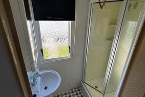 A bathroom with a white sink, a glass shower enclosure, and a patterned window. - Sleeps6-familyfriendly-cambersands-5mintobeach (Rye)
