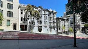 Katunäkymä, jossa on viktoriaaniseen tyyliin rakennettuja rakennuksia, punainen pyörätie ja opaste San Franciscon yliopistoon.