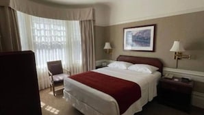 Una camera d'albergo con un letto, una sedia, un comodino, una lampada e una ventola a soffitto.