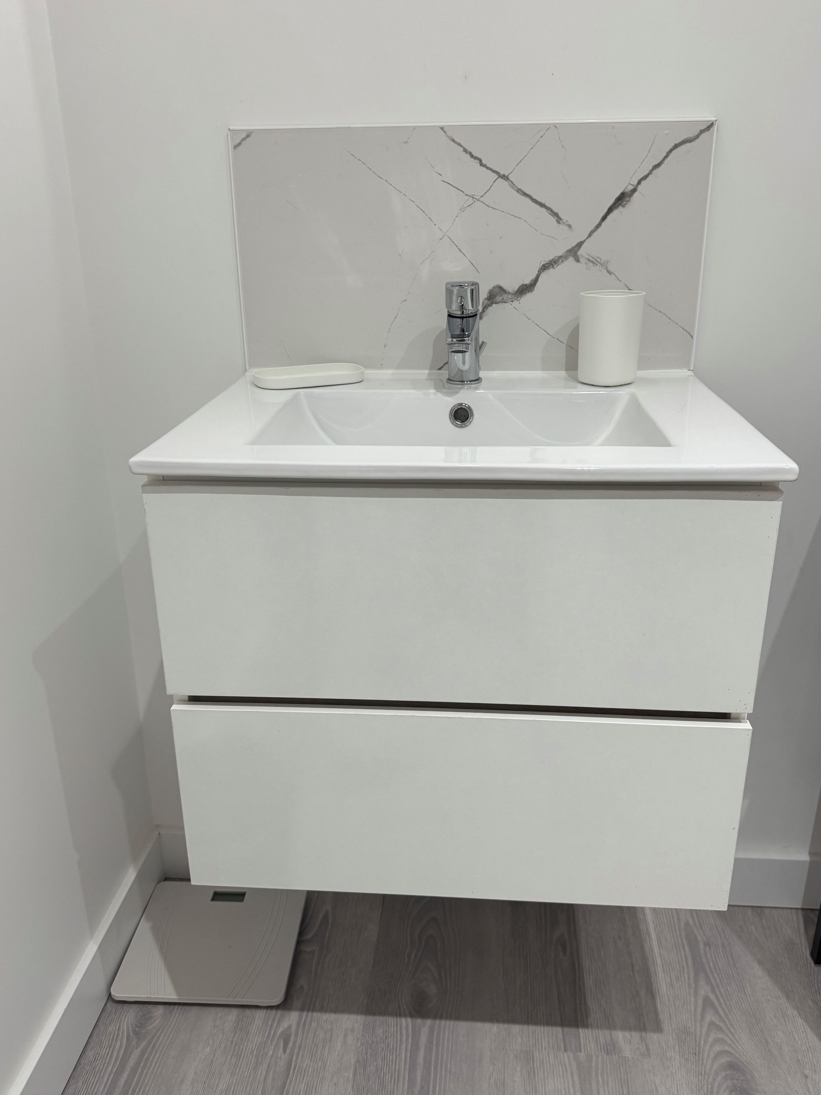 A white bathroom vanity with a marble backsplash, a sink, and a mirror.