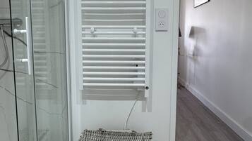 Ein Badezimmer mit Duschkabine aus Glas, einem weißen Handtuchhalter und einem Korbwäscheschrank auf dem Boden.