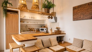 Une cuisine moderne avec des plans de travail en bois, un four encastré et un coin salon agrémenté de coussins en tissu tressé.