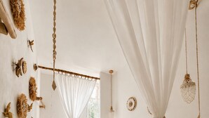 Une chambre à coucher avec un lit, une table de chevet, un luminaire suspendu et une fenêtre avec des rideaux.