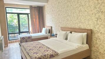 Habitación de hotel con una cama grande, una cama más pequeña, un balcón con cortinas y papel tapiz estampado.