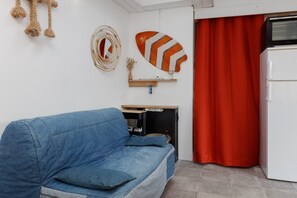 Ein gemütlicher Wohnraum mit einem blauen Sofa, einem kleinen Holztisch, einem weißen Kühlschrank und einem roten Vorhang.