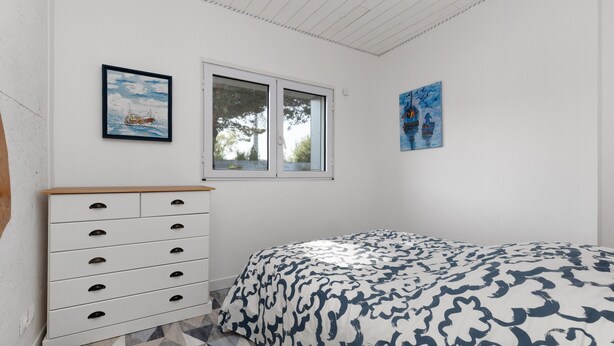 Un dormitorio con cama, cómoda, ventana y dos cuadros en la pared.