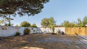 Un patio trasero con un muro blanco, una cerca de madera y una pequeña mesa con sillas.