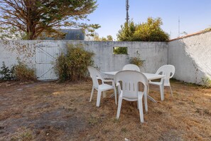 Une terrasse extérieure avec une table et des chaises, entourée d’un mur en béton, d’un portail en métal et de plantes.