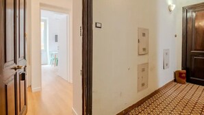 A hallway with a wooden door, a tiled floor, and a light switch on the wall. - Dante Art Studio (Roma)