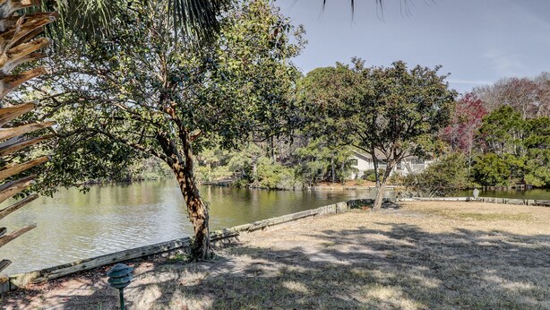 A serene park with a pond, trees, and a wooden dock. - Sunset Rentals | Queens Grant 616 | Dog Friendly (Hilton Head Island)