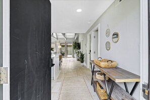 A hallway with a black door, a wooden bench with baskets, and a white wall with mirrors. - Sunset Rentals | Queens Grant 616 | Dog Friendly (Hilton Head Island)
