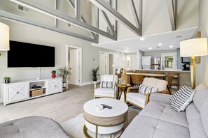 A modern living room with a flat-screen TV, a dining area with a kitchen in the background, and a staircase leading to an upper level. - Sunset Rentals | Queens Grant 616 | Dog Friendly (Hilton Head Island)