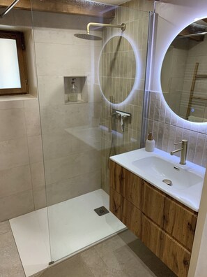 Ein modernes Badezimmer mit einer gläsernen Duschkabine, einem Holzwaschtisch, einem weißen Waschbecken und einem runden Spiegel.