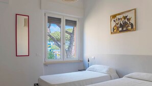 Quarto com duas camas, janela com vista, espelho e um quadro na parede.
