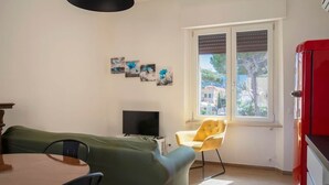 Um quarto com uma cama, televisão, janela com persianas e um armário vermelho.
