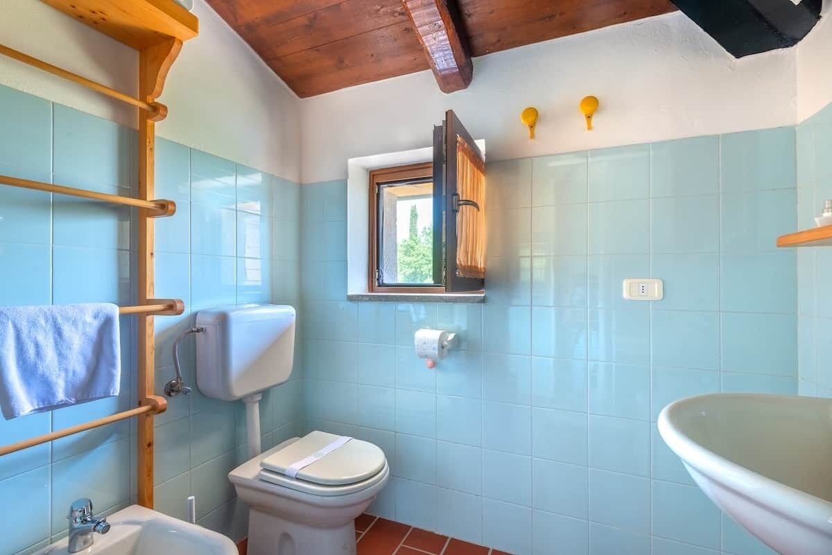 A bathroom with a toilet, sink, and window.