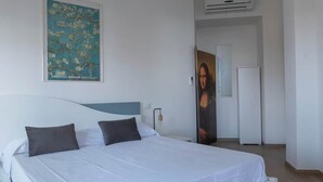 Een hotelkamer met een bed, een wandairconditioner en een deur die naar een andere kamer leidt.
