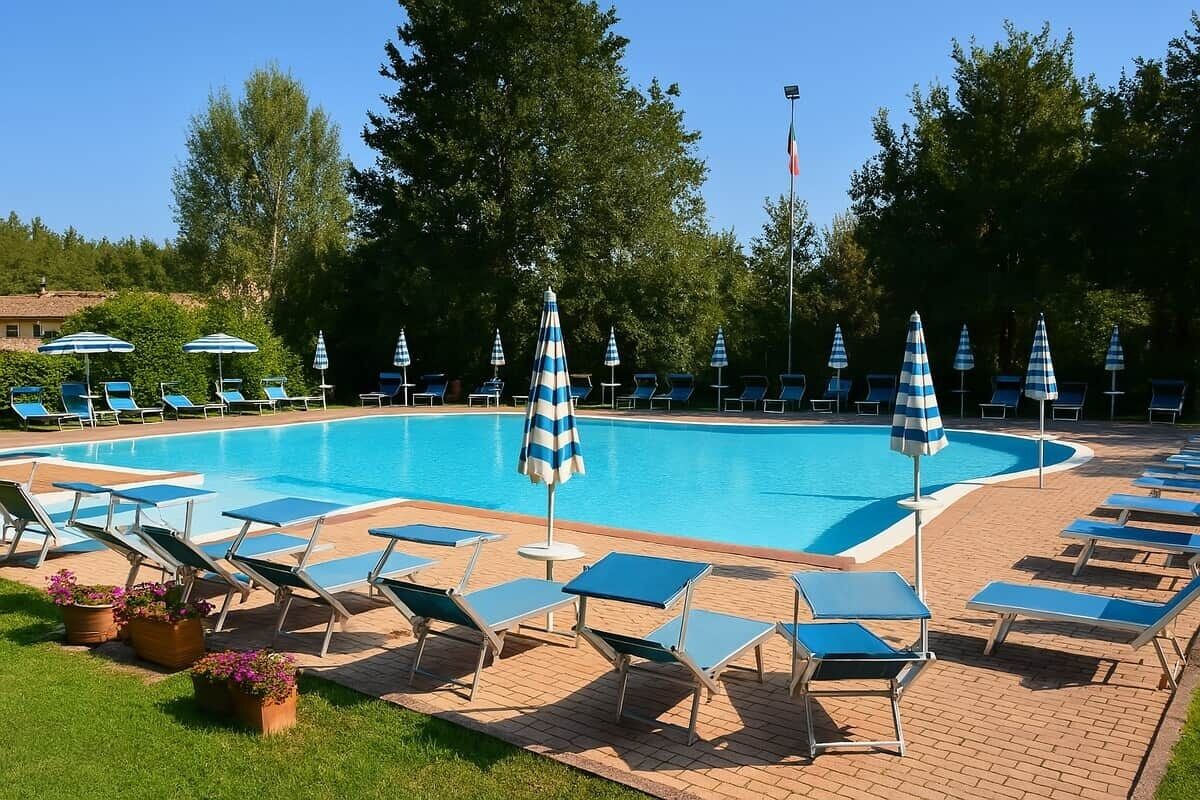 Una piscina con lettini e ombrelloni, circondata da alberi e un patio in mattoni.