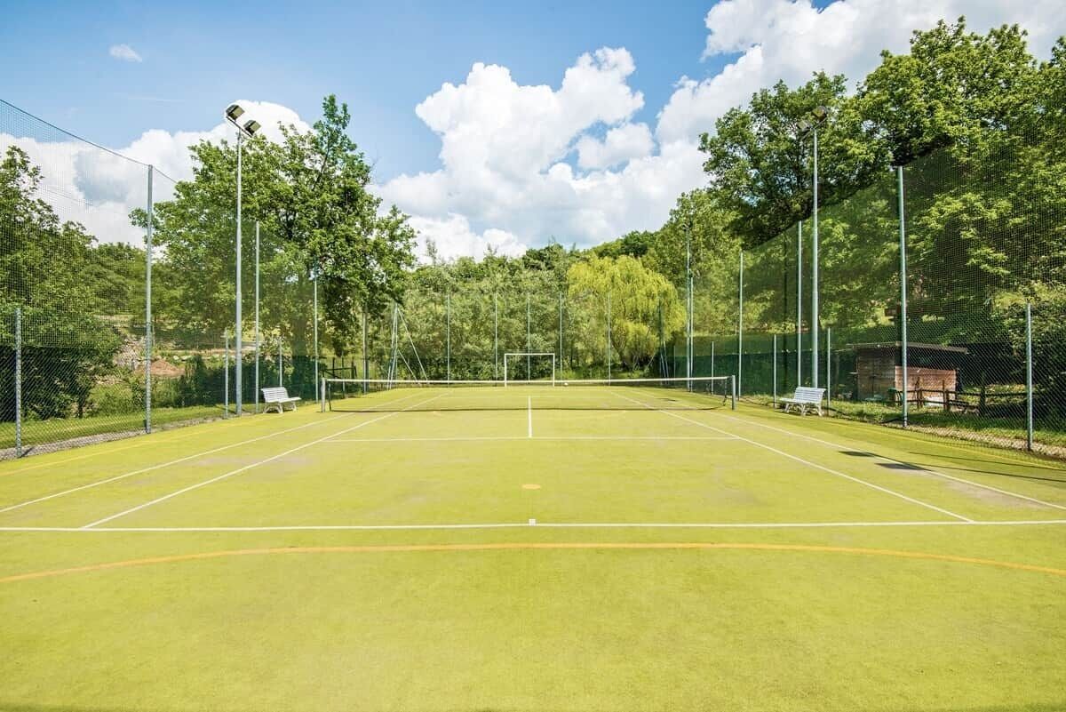 A tennis court with a net, surrounded by trees and a fence.