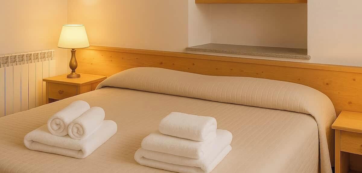 Una habitación de hotel con una cama, dos mesitas de noche, una lámpara y un radiador.
