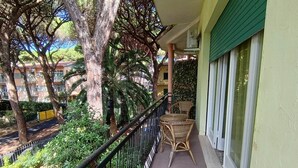 Ein Balkon mit Korbmöbeln, einem grünen Sonnensegel und Blick auf eine Wohngegend mit Bäumen und einem gelben Tor.