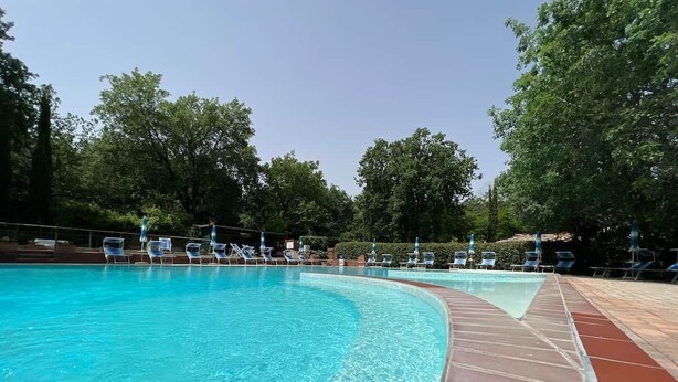 A swimming pool with clear blue water, surrounded by lounge chairs and a brick deck. - To complete (Castel del Piano)