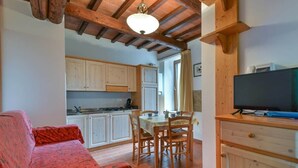 A cozy living area with a sofa, a dining table with chairs, a television, and a kitchen with cabinets and a stove. - To complete (Castel del Piano)