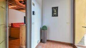 A hallway with a wooden ceiling, a potted plant, a framed picture on the wall, and a door leading to a room with a red bedspread. - To complete (Castel del Piano)