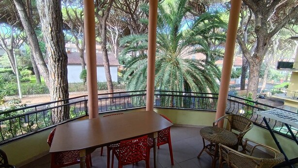 A covered balcony with a table and chairs, surrounded by trees and a view of a residential area. - 454 Orchidee Mare (3-seater) (Marina di Grosseto)