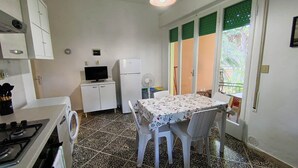 A compact kitchen with a gas stove, a washing machine, a refrigerator, a television, and a dining table with chairs. - 454 Orchidee Mare (3-seater) (Marina di Grosseto)