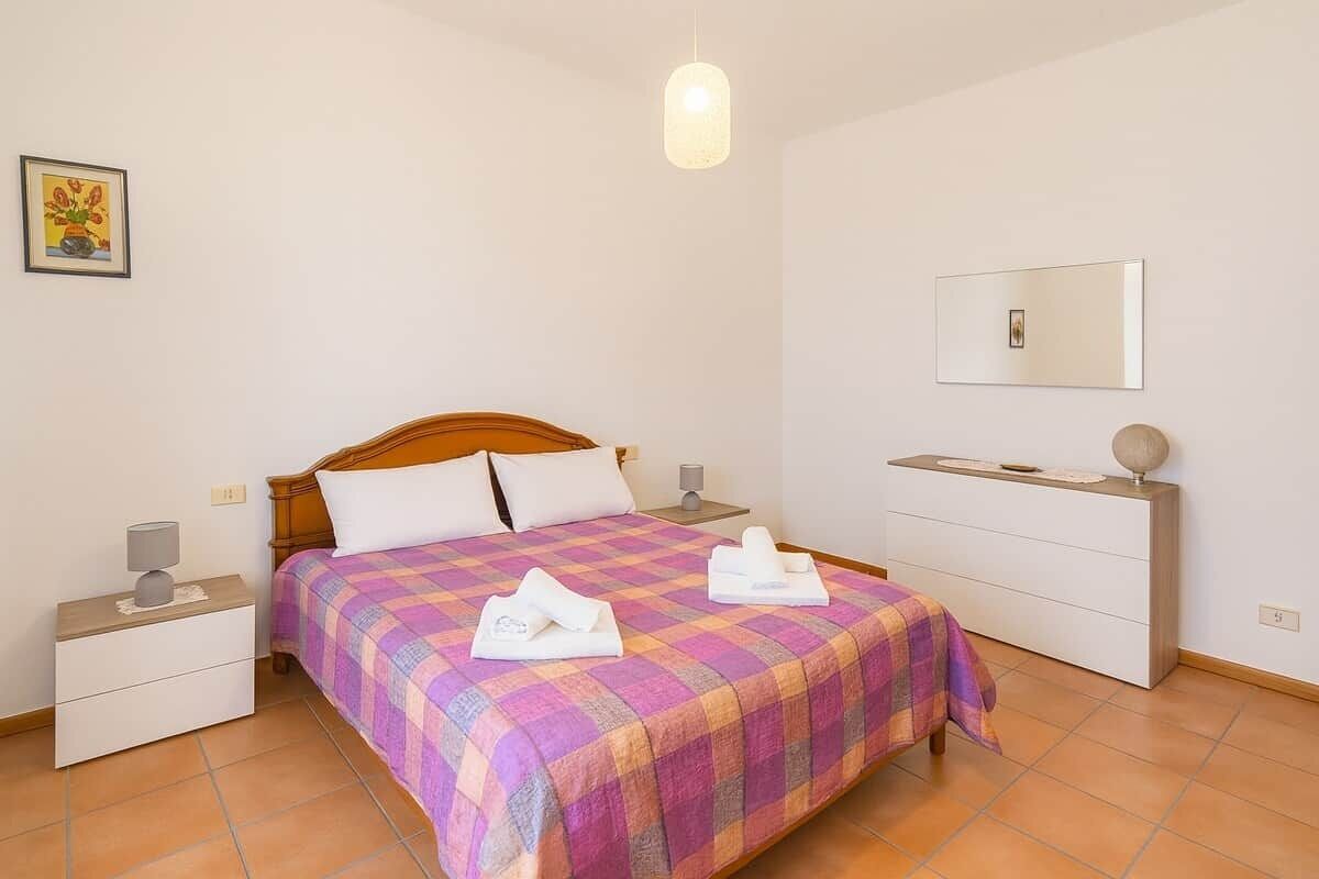 A neatly arranged bedroom with a bed, bedside tables, a dresser, and a hanging light fixture.